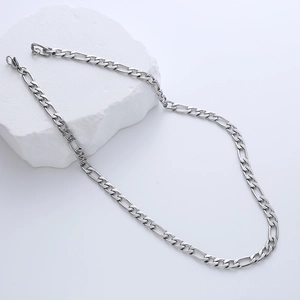 Detail shot of a silver Figaro chain necklace resting on a white gypsum stone block