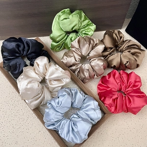 Set of eight assorted satin hair scrunchies displayed on a wooden tray with silk texture