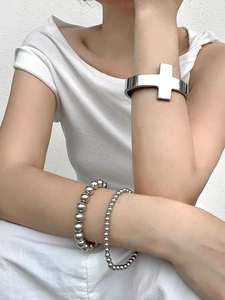 Detail of silver cross cuff bangle and beaded bracelets set on model's wrist