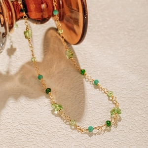 Close-up of bohemian gold chain with green gemstone beads and evil eye charm