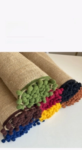 Detail of jute table runner featuring colorful pom-pom trim and reinforced edges