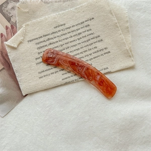 Detail of orange-brown marble patterned acetate hair clip on vintage fabric backdrop