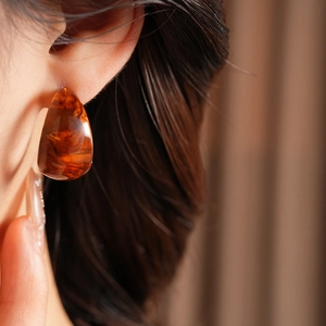 Detail of amber tortoiseshell resin C-shaped earring on model with glossy finish