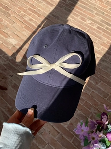 Detailed view of dark blue baseball cap with white satin bow decoration on red brick background