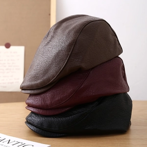 Three PU leather beret hats in brown, dark red, and black stacked on a wooden table