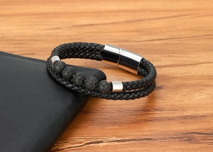 Detail shot of black braided leather bracelet with lava rock beads on a wooden desk