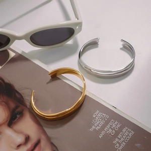 Gold and silver stainless steel open bangles displayed with sunglasses and magazine