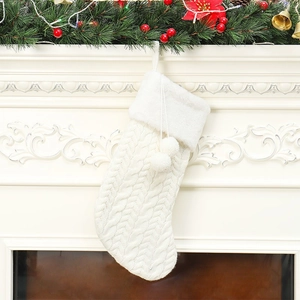 White cable knit Christmas stocking with pom-poms hanging on a festive mantelpiece decoration