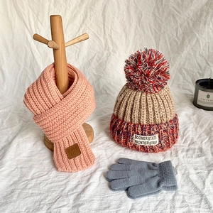 Cozy knit winter set for kids featuring a beige bobble hat, pink scarf, and grey gloves