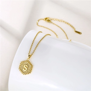 Close-up of hexagonal gold pendant with letter S engraving and beaded texture detail