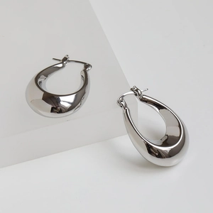 Detail of silver polished oval hoop earrings on a minimalist white stage with soft lighting