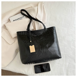 Close-up of black crocodile-embossed tote bag with elegant gold pendant detail