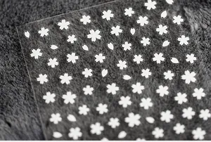 Detailed macro view of white cherry blossom 5D nail stickers on a grey textured surface