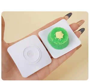 Close-up of a miniature green cake model on a square tray held by hand for size reference