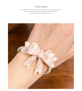 Detail of pearlescent pink acetate bow hair tie worn on wrist for size reference