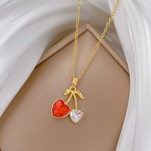 Close-up of golden cherry necklace with red and crystal heart gems on white silk
