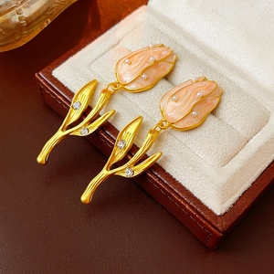Close-up of golden tulip earrings with pink enamel, white pearls and sparkling rhinestones