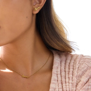 Close-up of a gold-plated 'love' script earring and necklace set on a female model