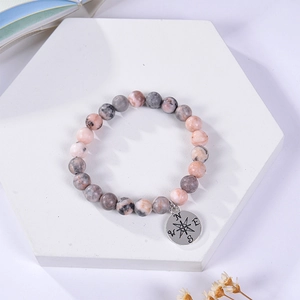 Pink and grey natural stone bead bracelet with silver compass pendant on white marble
