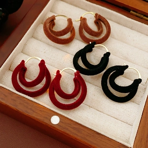 Gros plan de boucles d'oreilles en velours en C en marron, rouge et noir dans un écrin