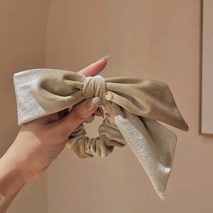 Detail of a beige velvet hair scrunchie with large bow and gold charm accessory
