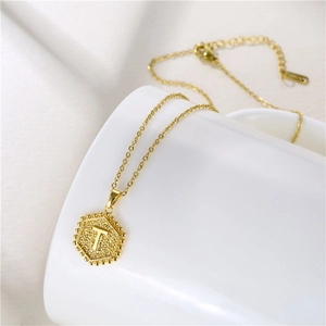 Macro detail of golden hexagonal letter T pendant necklace on white ceramic surface