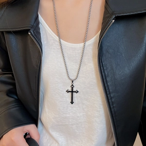 Detail shot of a black enamel cross pendant on a silver metal chain worn with a leather jacket