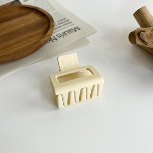 Detail of a square matte cream hair claw clip with cutout design on a wooden tray