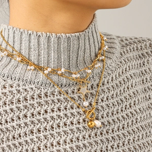 Close-up of layered gold star pendant necklace with white pearls and OT toggle clasp