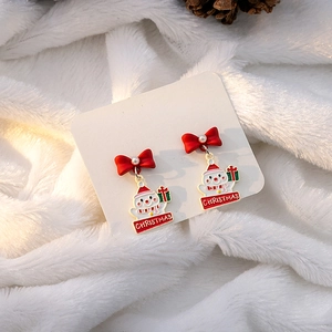 Detailed view of Christmas snowman earrings with red bow and faux pearl on fuzzy white surface