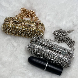 Mini rhinestone lipstick bags in gold and silver with metal chains on plush white background