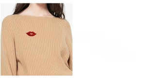 Detailed close-up of a vibrant red crystal-encrusted lip brooch on a beige knitted sweater