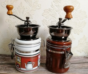 Manual coffee grinders with ceramic jars and metal cranks shown on a wooden tabletop