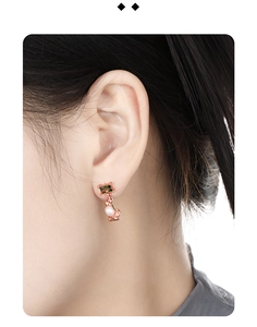 Detailed close-up of rose gold earrings with square green zircon and white pearls on ear