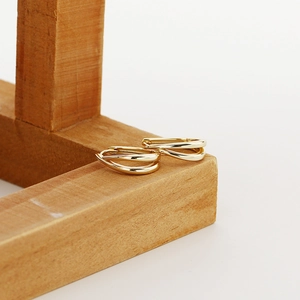Detail showing multi-layer gold twisted hoop earrings on a light wooden jewelry stand