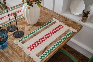 Close-up of woven festive placemat with red and green patterns and fringe on a wooden table