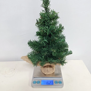 Mini artificial Christmas tree with burlap base being weighed on a digital scale