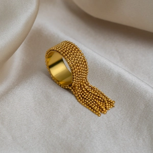 Close-up of a gold tassel beaded ring displayed on elegant champagne silk fabric