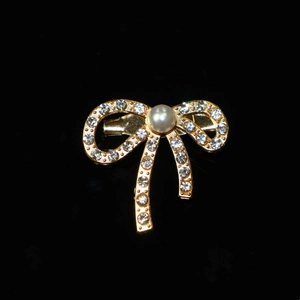 Macro view of gold bow brooch with inlaid rhinestones and centered large white pearl