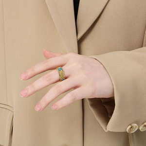 Detail of gold enamel crossover ring with braided edges worn with a beige blazer