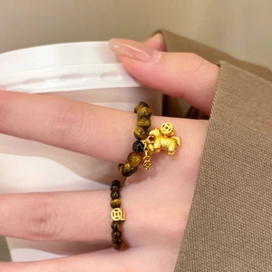 Tiger eye beaded rings with a golden pig charm and copper coin on a model's hand