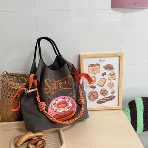 Detail of grey nylon tote bag with sweet donut embroidery and orange shoulder strap