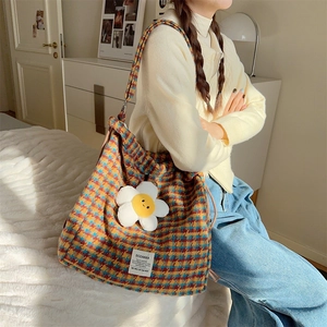 Side view of a large plaid canvas tote bag featuring a sunflower plush charm on a woman