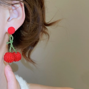 Detailed close-up of beaded cherry earrings with red pom-pom studs on model
