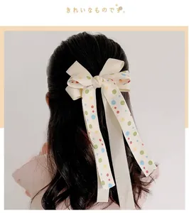Detail of a large creamy white bow hair clip with colorful dots and long ribbons for girls