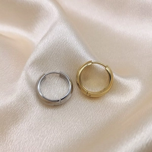 Minimalist thick hoop earrings in gold and silver finish on soft beige silk fabric