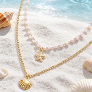 Dettaglio collana a strati dorata con perle rosa, stella marina e ciondolo a conchiglia