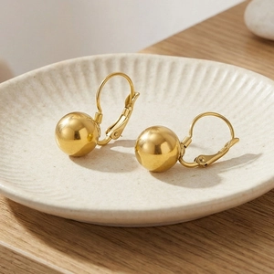 Detailed view of polished gold stainless steel sphere earrings on a ceramic dish