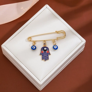 Detailed view of evil eye and hand of Fatima charms on a golden brooch in a gift box