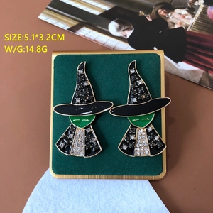 Detail view of cartoon witch earrings with black enamel and green gems on velvet display